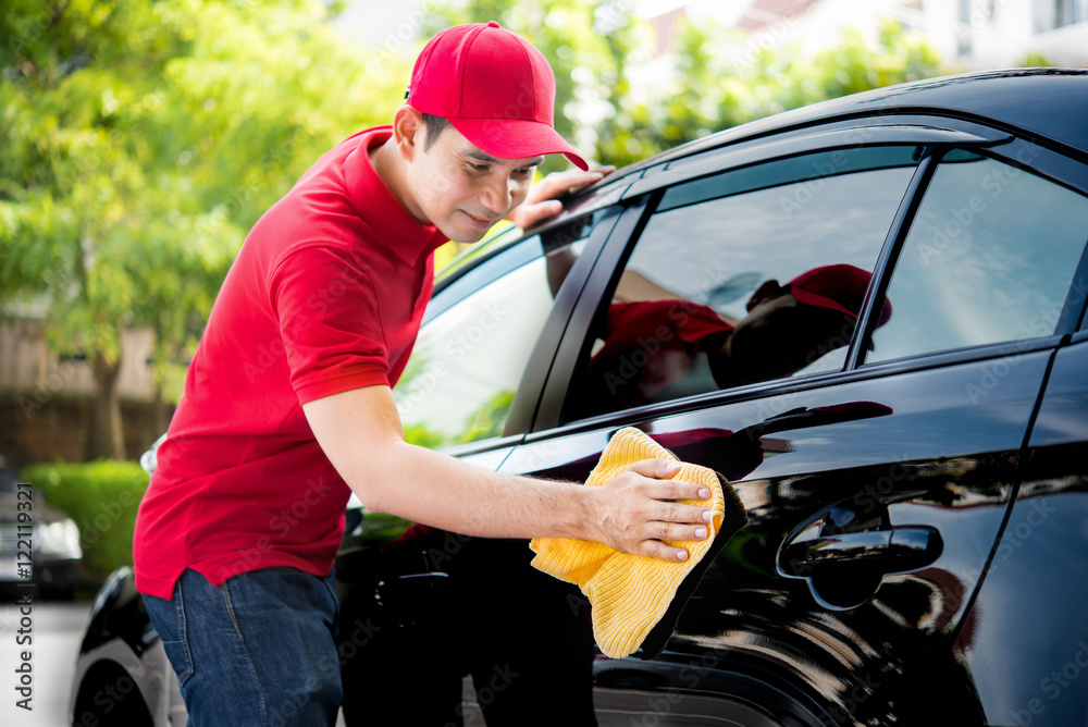 Auto service staff in red uniform cleaning car with microfiber cloth