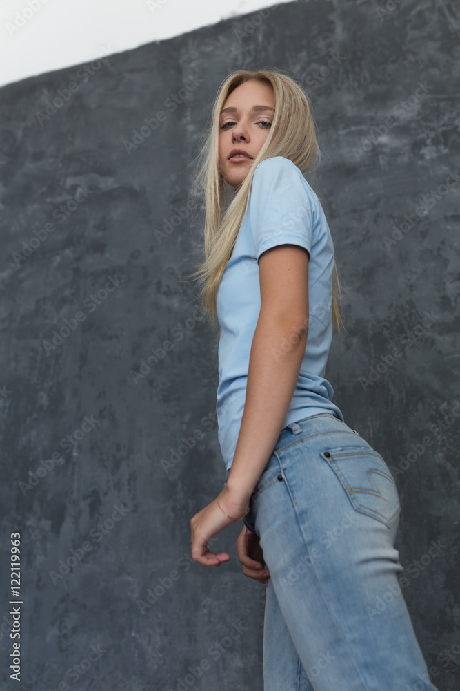 Portrait of a blonde in a blue T-shirt and jeans with her hair and natural makeup