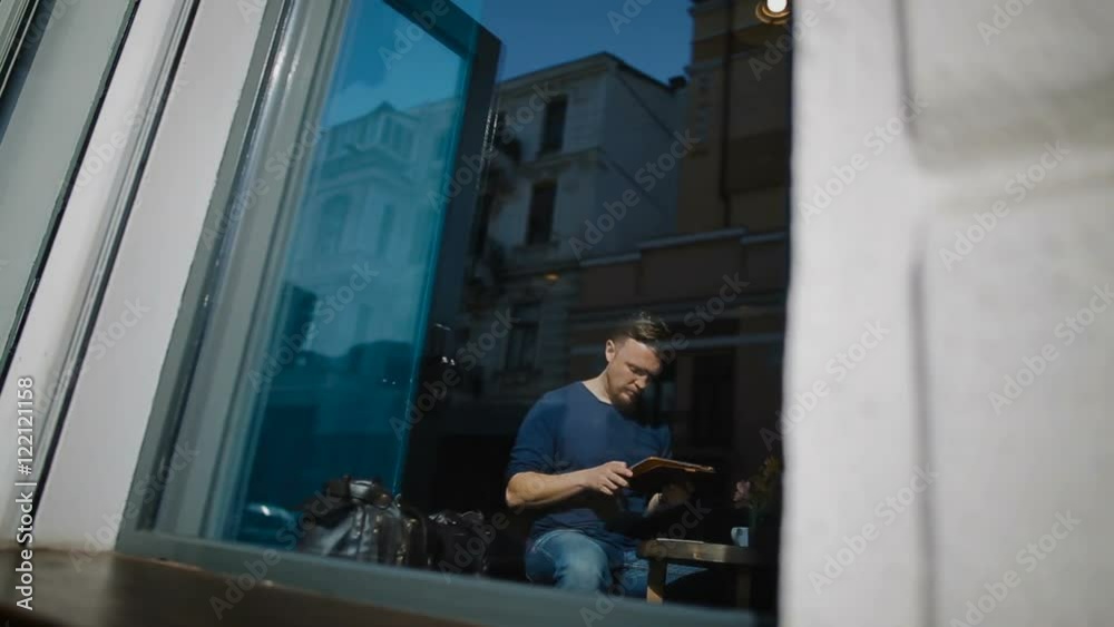 The young man sits in cafe and works with the tablet The young man sits in cafe and works with the tablet