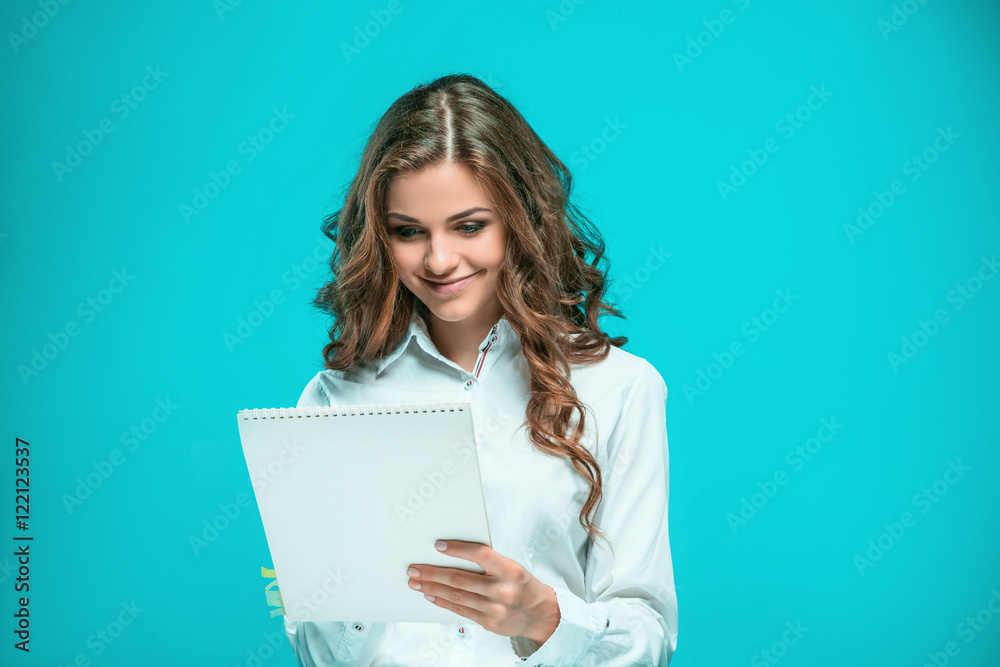 The smiling young business woman with pen and tablet for notes on blue background The smiling young business woman with pen and tablet for notes on blue background