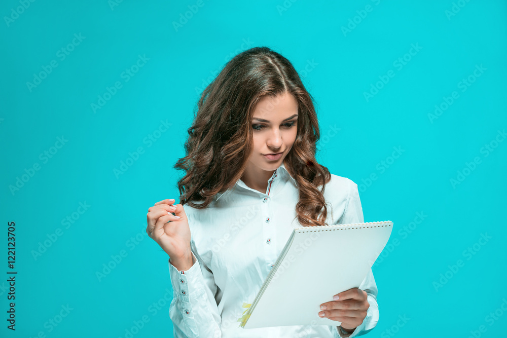 The smiling young business woman with pen and tablet for notes on blue background The smiling young business woman with pen and tablet for notes on blue background