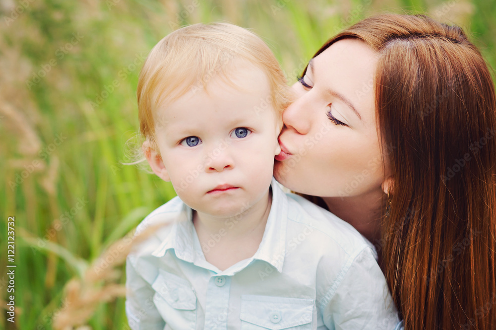 Mom tenderly kissing baby son in the ear, nature, close-up. Mom tenderly kissing baby son in the ear, nature, close-up.