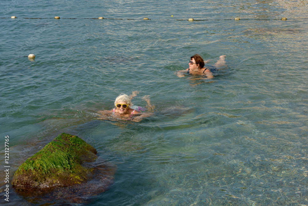 Two women are swimming in clear water of sea shallow.