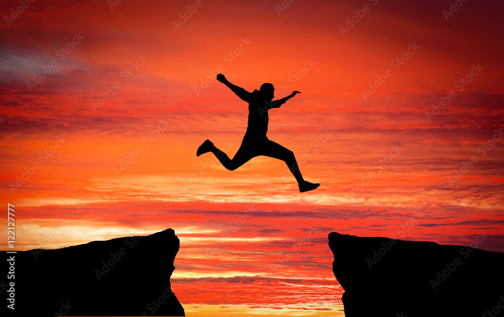 Fototapeta premium Man jumping across the gap from one rock to cling to the other.