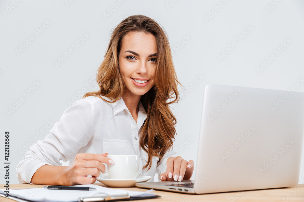 Smiling pretty young businesswoman drinking coffee and working with laptop Smiling pretty young businesswoman drinking coffee and working with laptop