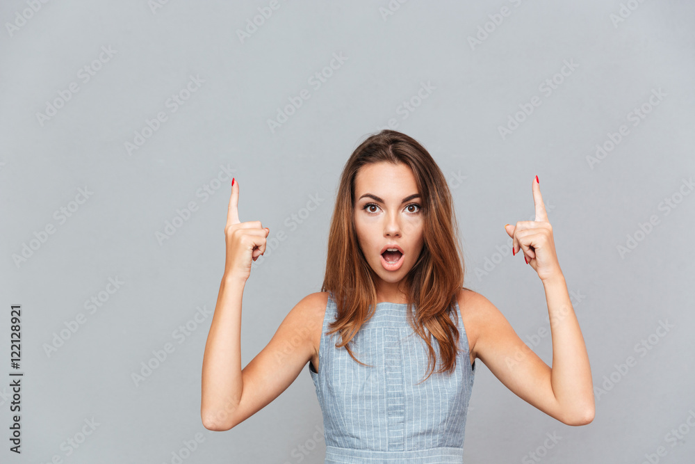 Amazed shocked young woman pointing up with both hands