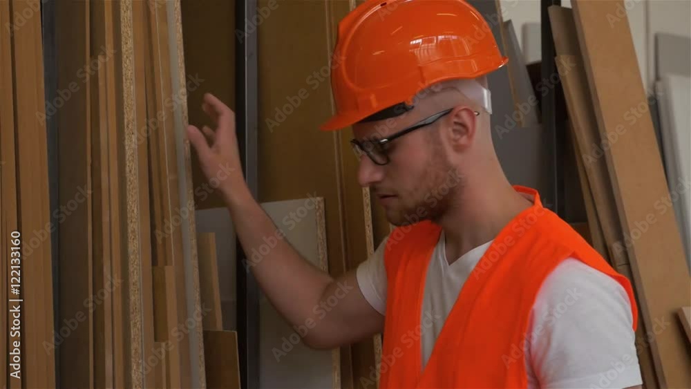 Young carpenter is counting wooden desk and using tablet pc. Carpentry shop background Young carpenter is counting wooden desk and using tablet pc. Carpentry shop background