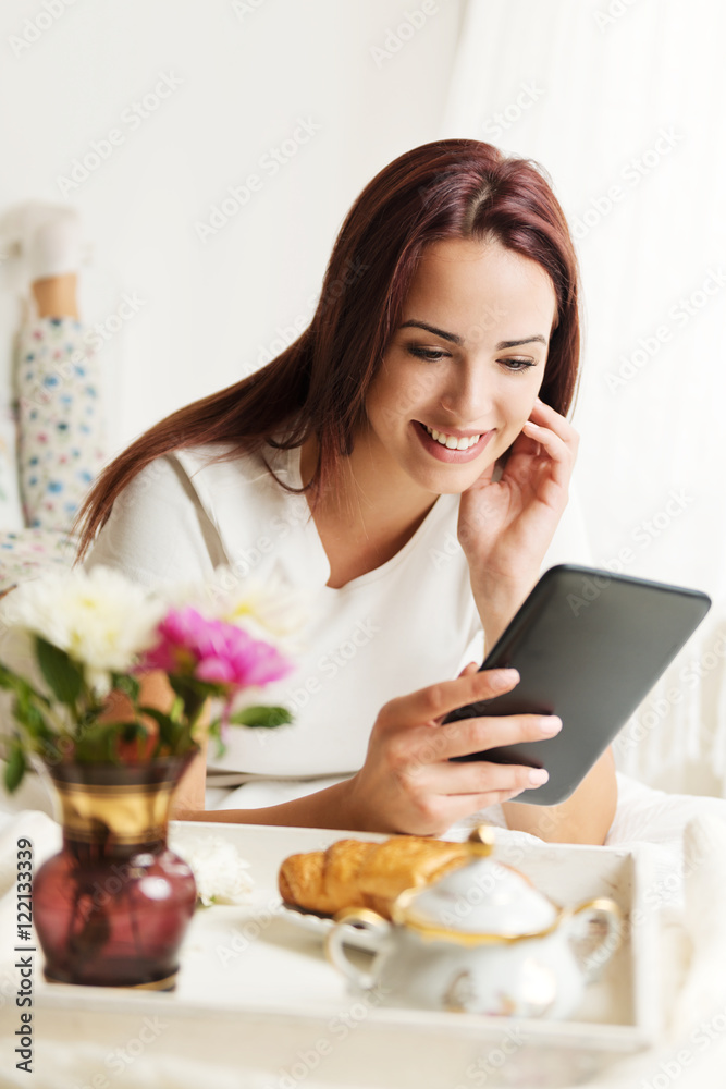 Beautiful woman using a tablet in a bright room with breakfast in bed