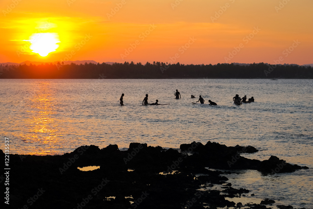 Surfers Waiting For Waves in the Water During Orange Siargao Island Sunset - Philippines