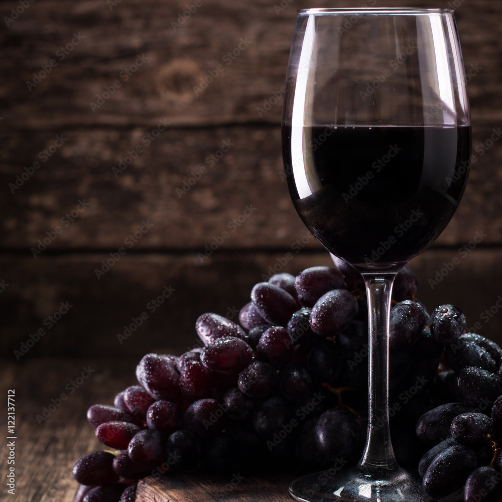 Glass of red wine, served with grapes on a wooden background