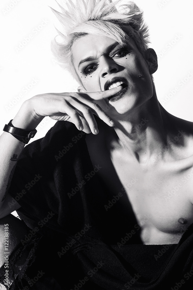 Freaky gothic fashion model boy with blonde hair, piercing and black make up in black mantle