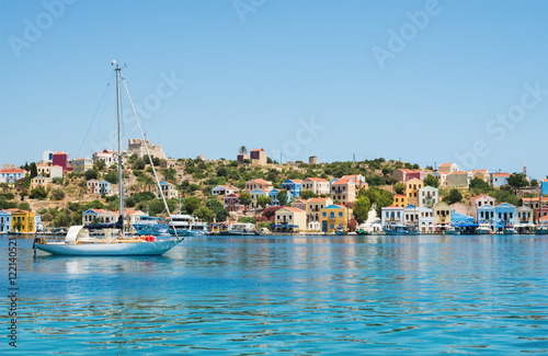 View over bay of Kastelorizo on sunny summer day. Island coast with typical colorful Greek houses, clear turquoise sea water and yacht. Dodecanese, Greece