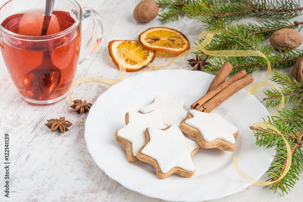 Close up of homemade butter nuts star shaped cookies with icing, pine, orange slices,cinnamon, anise, walnuts and golden ribbon over white wood background. A cup of berry tea. Christmas decoration.
