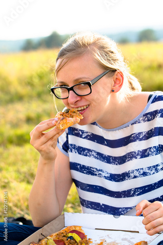 Smiling woman eating pizza outdoors, picnic and relax on meadow