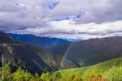 mountain landscape pine trees near valley and colorful forest on hillside under blue sky with clouds and rainbow