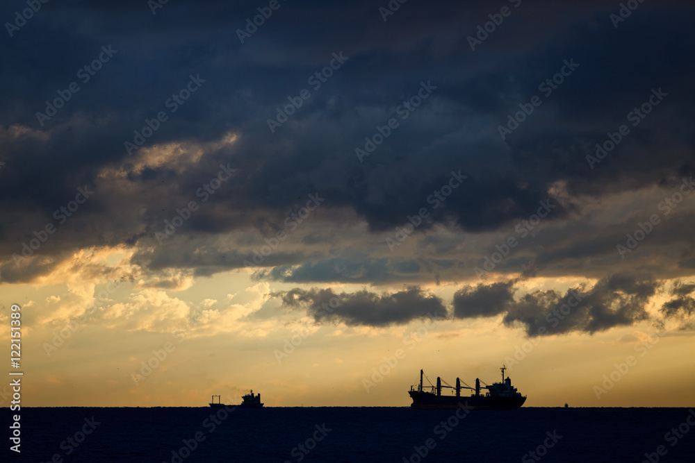 Cargo ships on sea in the rays of the setting sun and dramatic clouds