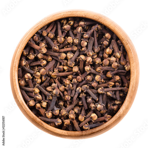 Dried cloves in a wooden bowl on white background. Brown aromatic flower buds of Syzygium aromaticum, commonly used as spice, in beverages or in herbal medicine. Isolated macro food photo close up.