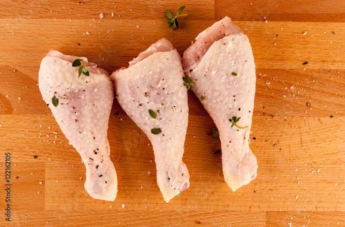 Organic raw chicken drumsticks on wooded board with herbs and spices