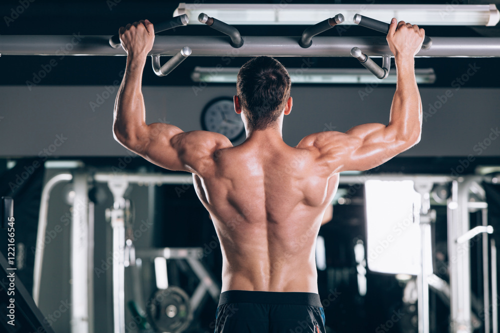 Athlete muscular fitness male model pulling up on horizontal bar in a gym Athlete muscular fitness male model pulling up on horizontal bar in a gym