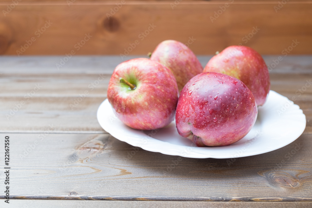 Four fresh red apples in white plate on wooden background Four fresh red apples in white plate on wooden background