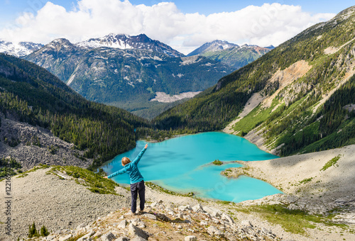 Young hiker woman standing on a cliff of mountain and have a fun. Amazing panoramic view of Wedgemount lake British Columbia Canada. Concept of freedom, beautiful healthy enjoying life.
