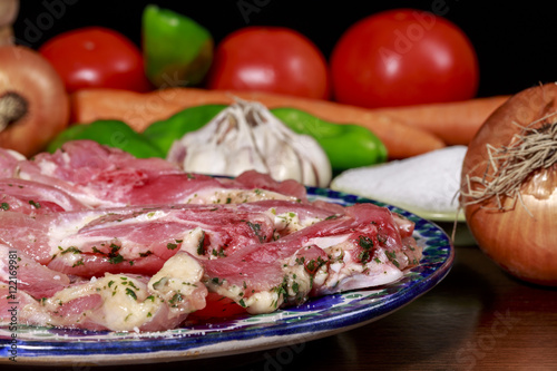 Detail of dish with turkey raw meat marinated with garlic and parsley beside salt dish, garlic bulb, onions and other vegetables