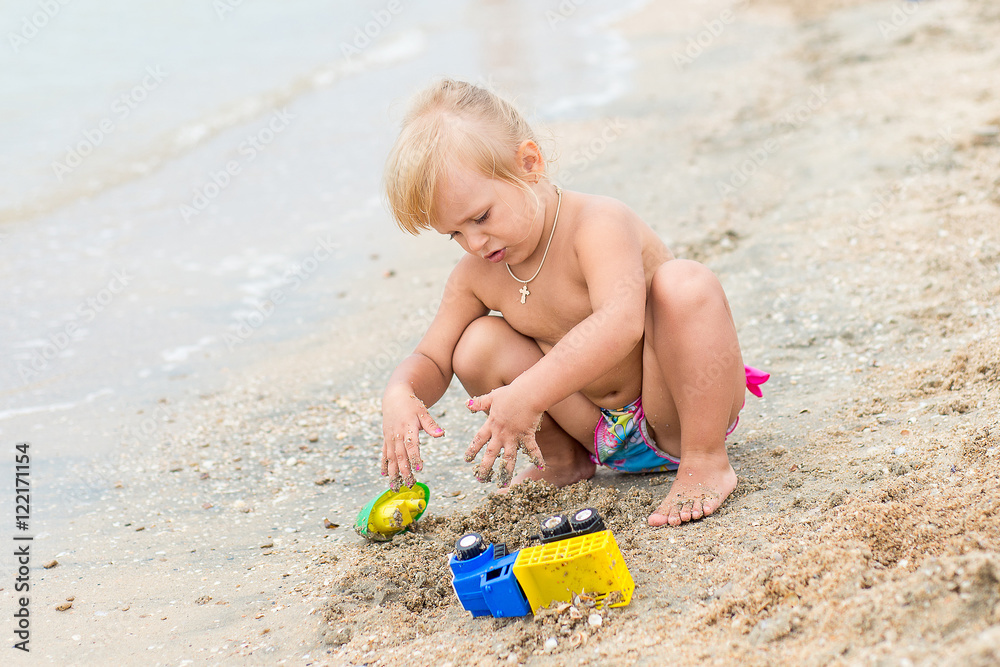 Adorable toddler girl playing with beach toys on white sand beach Adorable toddler girl playing with beach toys on white sand beach