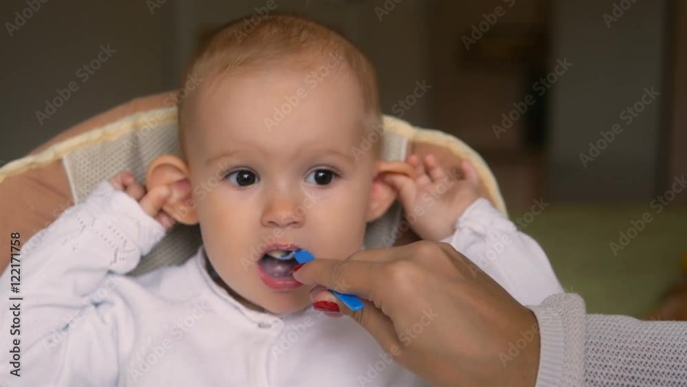 Little girl eating yogurt in Child seat and smiling. Happy family concept. Mother with spoon and baby food.