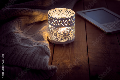 Cozy winter night knitted sweater candle and bookreader on wood surface photo