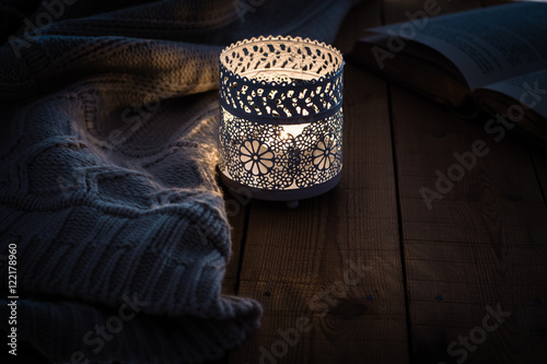 open book burning candle and knitted sweater on wood table on cozy winter night