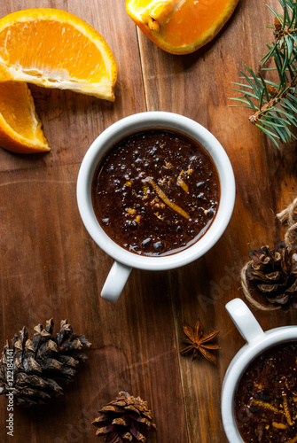Hot chocolate with spices  orange and orange zest. Against the background of Christmas tree branches  cones and orange. Wooden table  top view