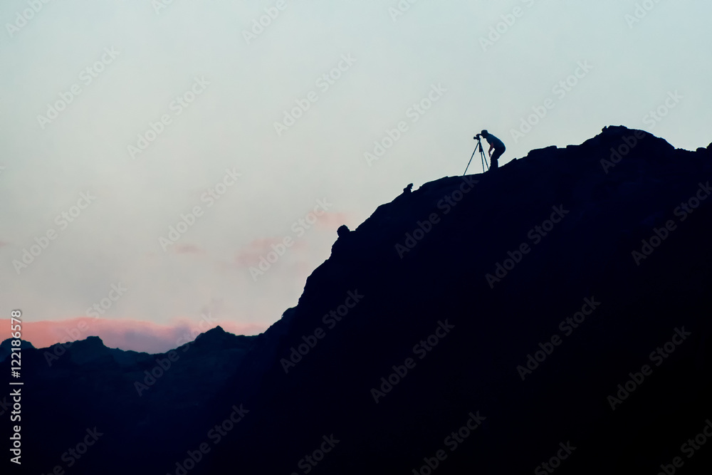 Silhouette of photographer on jagged rocky cliff taking sunrise