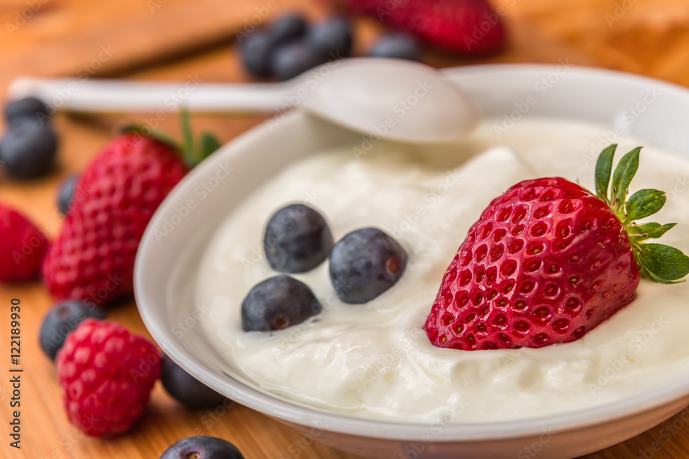 strawberries and blueberries, some of in yogurt and on wooden tr strawberries and blueberries, some of in yogurt and on wooden tr