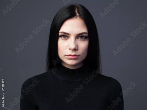 Beautiful serious woman with sad look, gray background photo