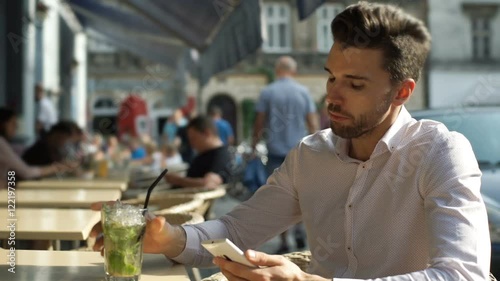 Handsome man drinking refreshing mojito and browsing internet on smartphone
 photo