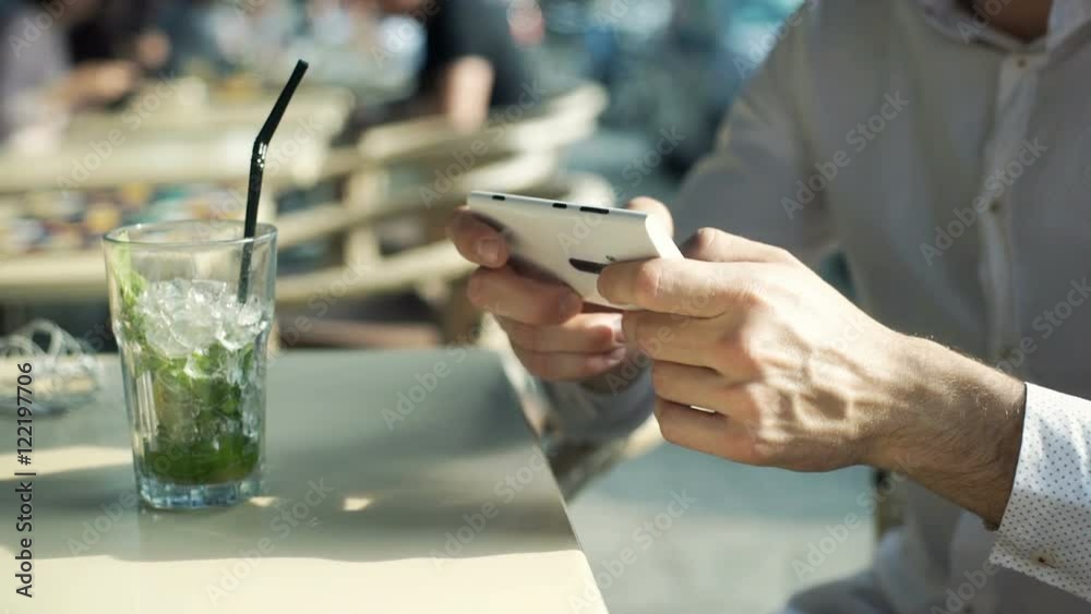 Man drinking mojito and texting on smartphone while sitting in the outdoor cafe
Man drinking mojito and texting on smartphone while sitting in the outdoor cafe