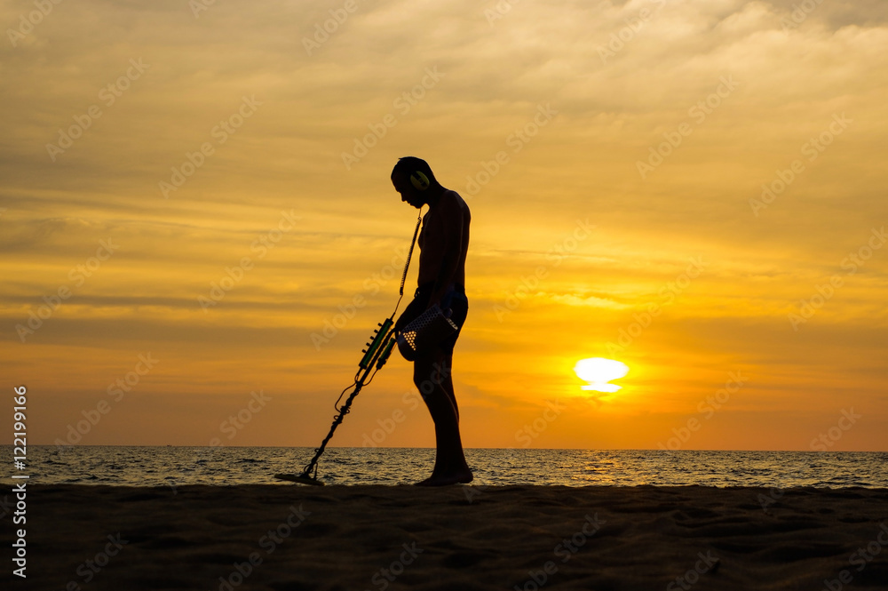 Treasure hunter with Metal detector on sunset the beach