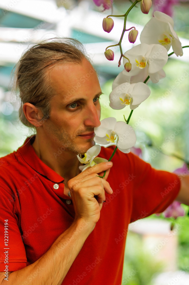 Handsome young man in garden smelling beautiful flowers in a sunny day Handsome young man in garden smelling beautiful flowers in a sunny day