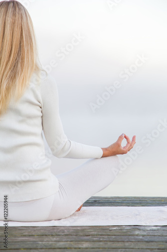 Woman wearing white clothes relaxing and practicing yoga in the mist on the lake footbridge early morning. Focus point on the hand.