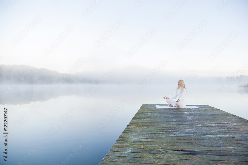 Woman relaxing and practicing yoga in the mist on the lake footbridge early morning. White clothes. Woman relaxing and practicing yoga in the mist on the lake footbridge early morning. White clothes.