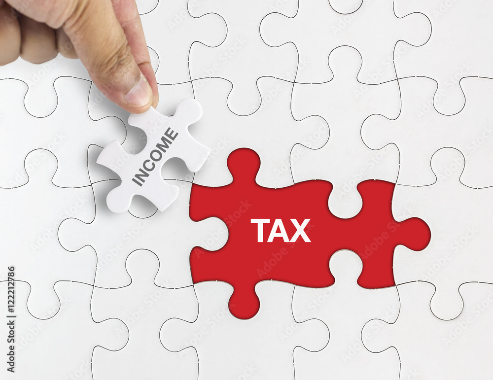 Hand holding piece of jigsaw puzzle with word INCOME TAX Hand holding piece of jigsaw puzzle with word INCOME TAX
