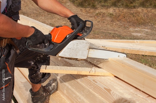 Construction Worker Cutting Beam with saw. Workers cutting timber wood with chainsaw. Saw sawing timber.   © martinfredy