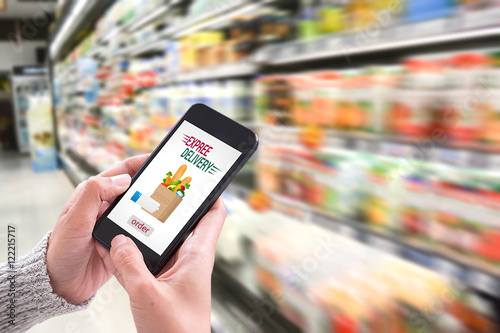 Hand holding smartphone with delivery service app on screen and fresh food supermarket store background