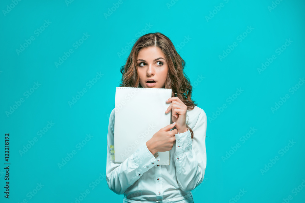 The thoughtful young business woman with pen and tablet for notes on blue background The thoughtful young business woman with pen and tablet for notes on blue background