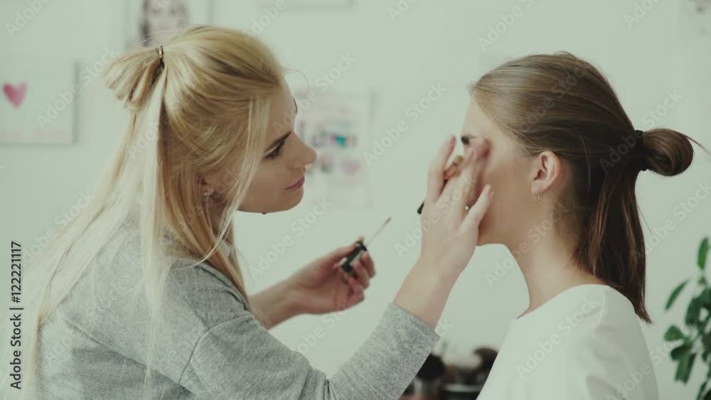 Make-up work. Make-up artist and model. Makeup. Girl makeup with long white hair. Makeup artist applies eye shadow to model. Make-up artist makeup girl s eye using a paint brush.
