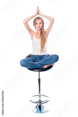 Vertical shot of a young beautiful long haired woman meditating seated on an office or bar chair isolated on white background.