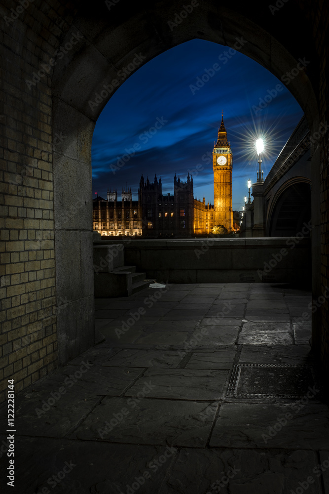 Brick tunnel overlooking Big Ben and the Houses of Parliament at night from across the river Thames and Westminster bridge southbank in London, England, UK