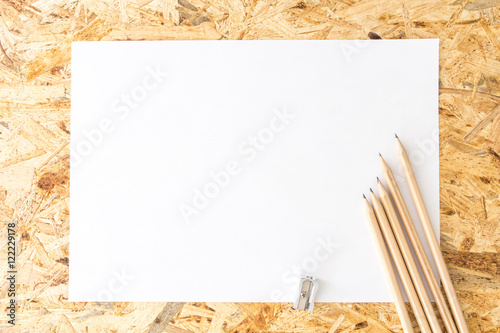 Bunch of pencils with sharpener, on blank white sheet of paper, on flakeboard