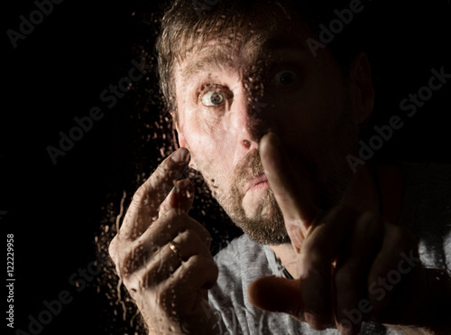 Drops of water on a glass, hand and male face. adult man standing at the window in rainy day.