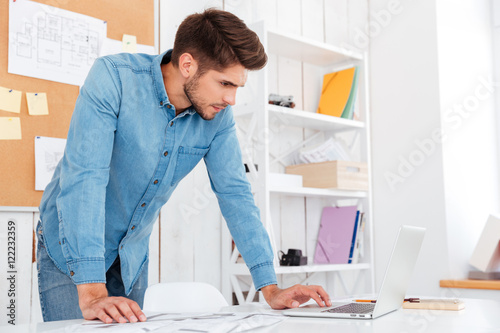 Pensive young businessman using laptop while standing in office